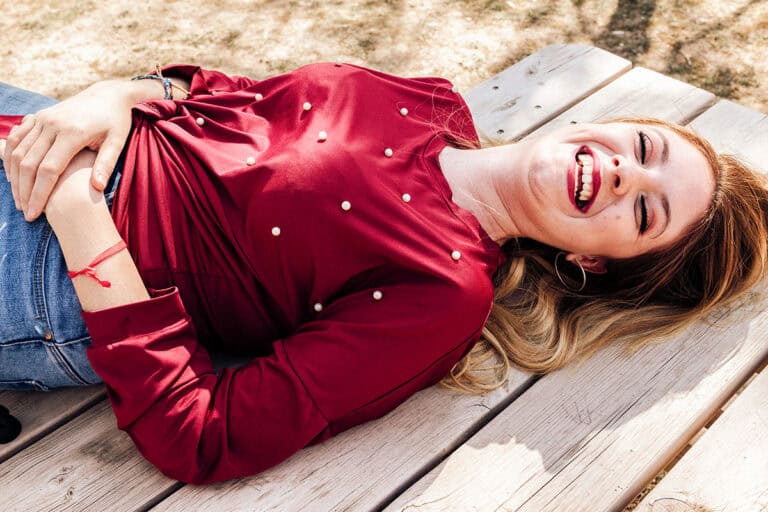 Smiling middle aged woman laying on her back on top of a picnic table outdoors