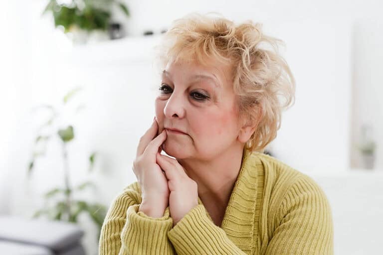Mature woman sitting with her hands at her chin lost in thought