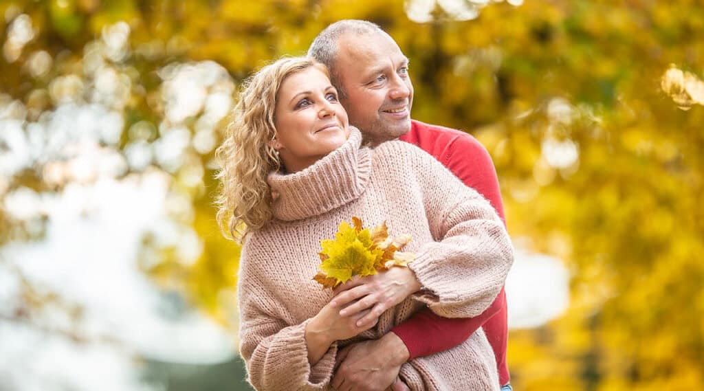 Happy middle aged couple embraced holding fall leaves outdoors